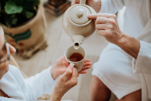 Close-up of senior couple in bathrobes pouring a hot tea, calm and hygge atmosphere.