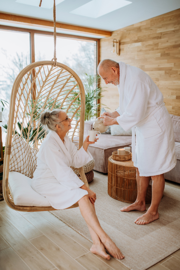 Senior couple in bathrobes enjoying time together in their living room, drinking a hot tea, calm and hygge atmosphere.