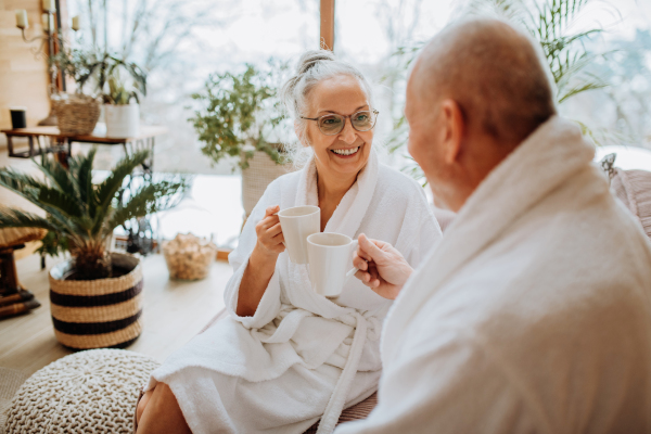 Senior couple in bathrobes enjoying time together in their living room, drinking a hot tea, calm and hygge atmosphere.