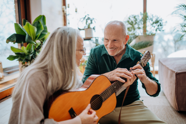 Senior couple playing on guitair, sitting in a cozy living room and enjoying autumn day.