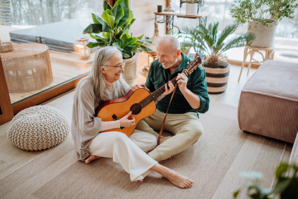 Senior couple playing on guitair, sitting in a cozy living room and enjoying autumn day.