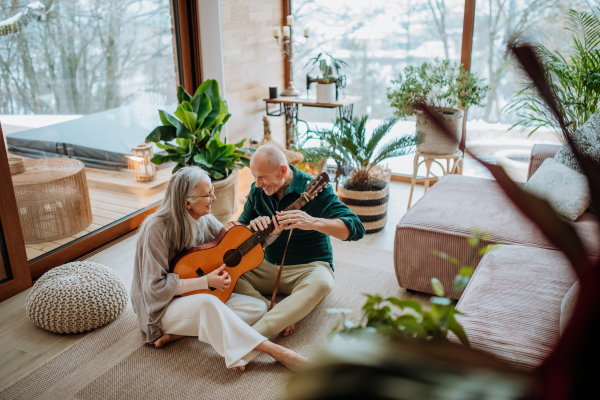 Senior couple playing on guitair, sitting in a cozy living room and enjoying autumn day.