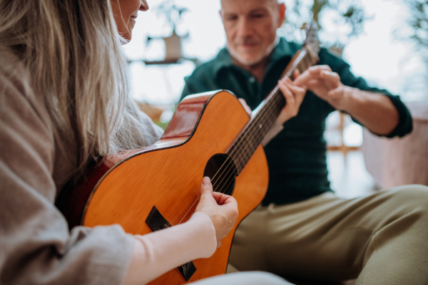 Senior couple playing on guitair, sitting in a cozy living room and enjoying autumn day.