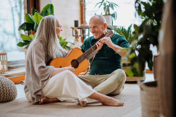 Senior couple playing on guitair, sitting in a cozy living room and enjoying autumn day.