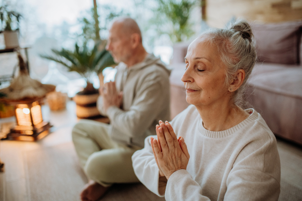 Senior couple meditating together in their living room during a cold autumn day.