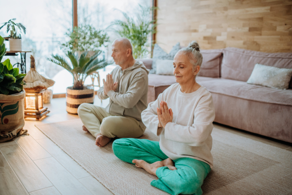 Senior couple meditating together in their living room during a cold autumn day.