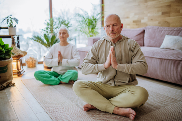 Senior couple meditating together in their living room during a cold autumn day.