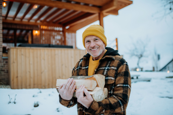 Senior man carrying wooden logs for preparing outdoor fire, during a winter day.