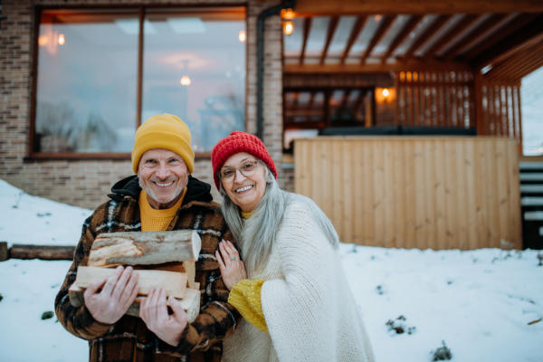 Portrait of senior couple carrying wooden logs and preparing outdoor fire, during a winter day.