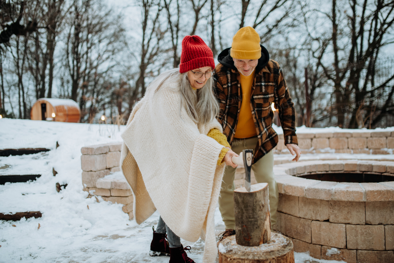 Senior couple chopping wood together in front of their house, during a cold winter day.