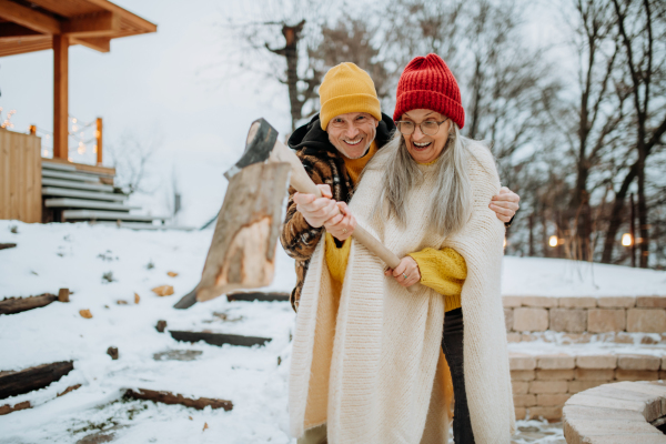 Senior couple chopping wood together in front of their house, during a cold winter day.