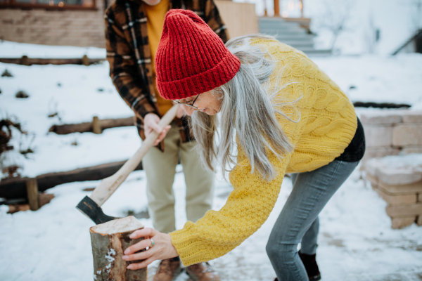 Senior couple chopping wood together in front of their house, during a cold winter day.