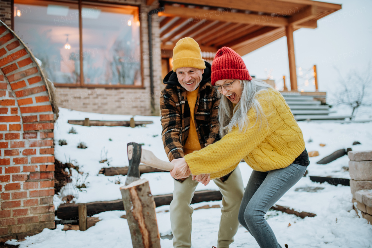 Senior couple chopping wood together in front of their house, during a cold winter day.