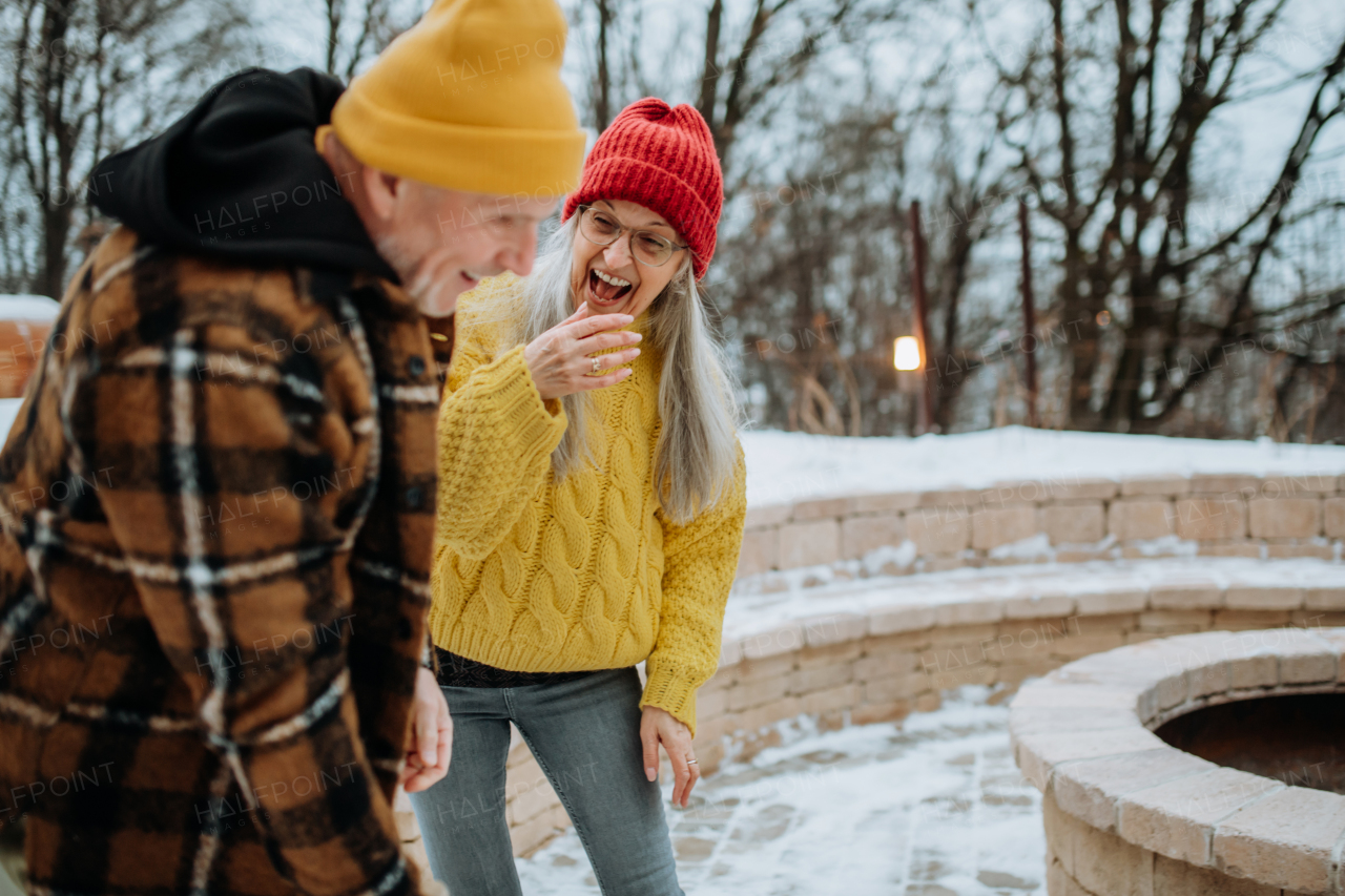 Senior couple having fun and chopping wood together in front of their house, during a cold winter day.