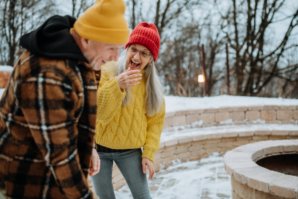 Senior couple having fun and chopping wood together in front of their house, during a cold winter day.