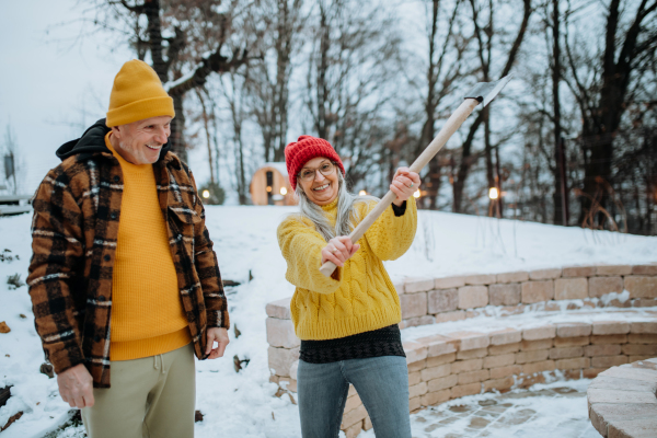 Senior couple chopping wood together in front of their house, during a cold winter day.