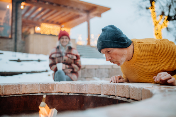 Senior couple sitting and heating together at outdoor fireplace during winter evening.