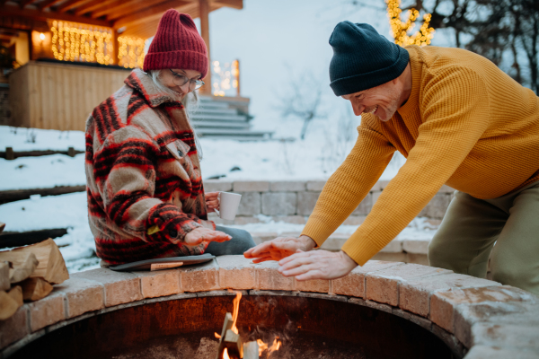 Senior couple sitting and heating together at fireplace in their winter garden.