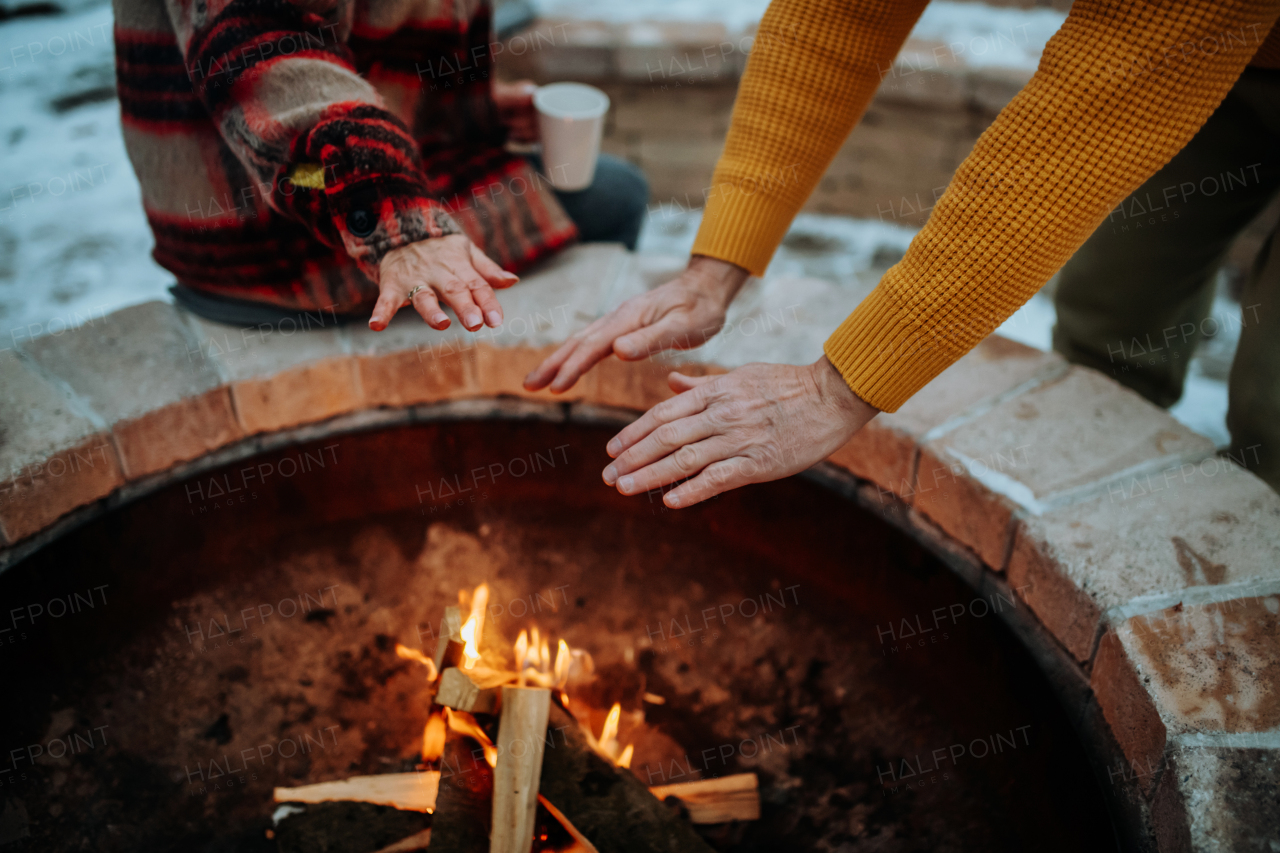 Senior couple sitting and heating together at outdoor fireplace during winter evening.