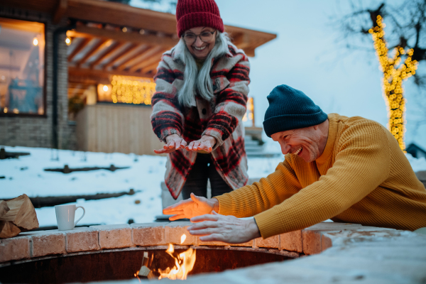 Senior couple sitting and heating together at outdoor fireplace during winter evening.