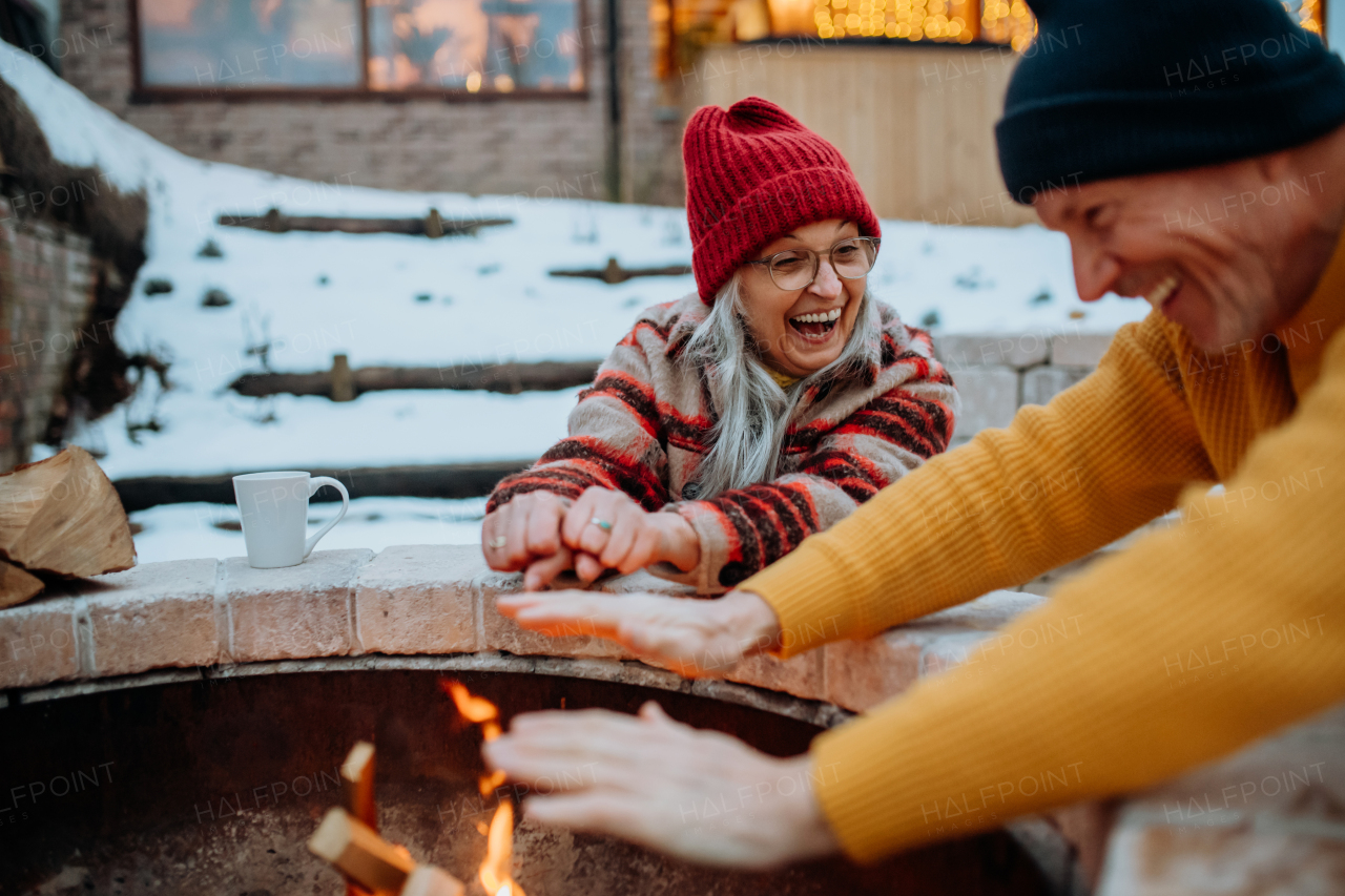 Senior couple sitting and heating together at outdoor fireplace during winter evening.