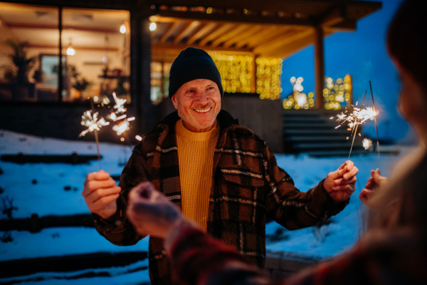 Happy senior couple celebrating new year with the sparklers, enjoying winter evening.