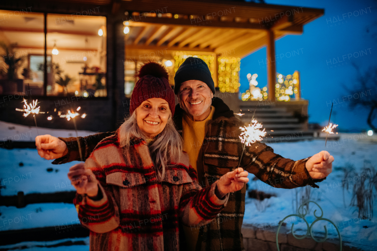 Happy senior couple celebrating new year with the sparklers, enjoying winter evening.