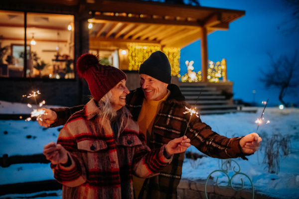 Happy senior couple celebrating new year with the sparklers, enjoying winter evening.