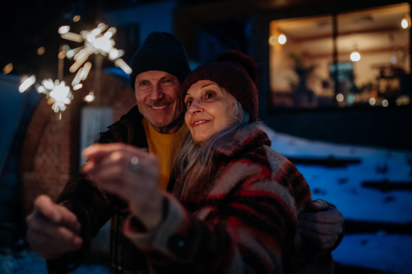 Happy senior couple celebrating new year with the sparklers, enjoying winter evening.