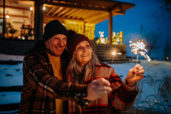 Happy senior couple celebrating new year with the sparklers, enjoying winter evening.