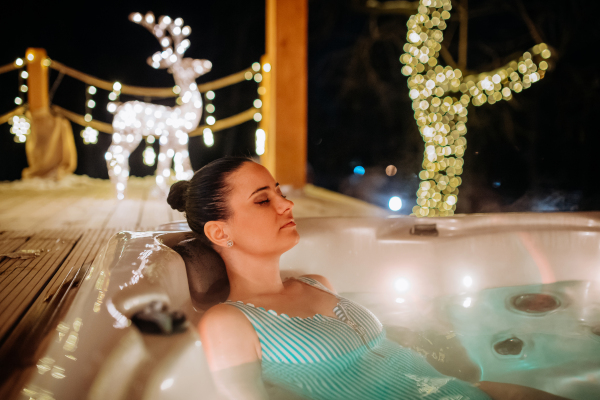 Young woman enjoying outdoor bathtub in her terrace during a cold winter evening.