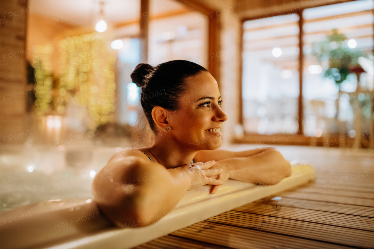 Young woman enjoying outdoor bathtub in her terrace during a cold winter evening.