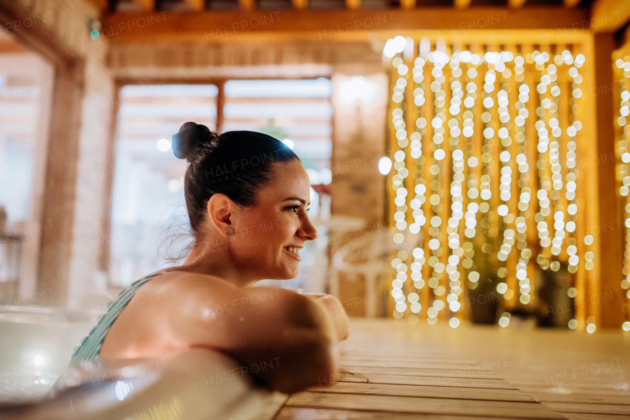 Young woman enjoying outdoor bathtub in her terrace during a cold winter evening.