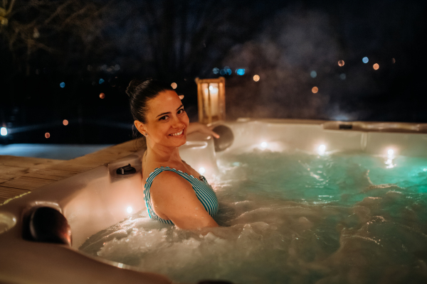 Young woman enjoying outdoor bathtub in her terrace during a cold winter evening.