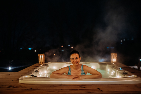 Young woman enjoying outdoor bathtub in her terrace during a cold winter evening.