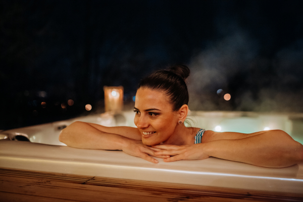 Young woman enjoying outdoor bathtub in her terrace during a cold winter evening.