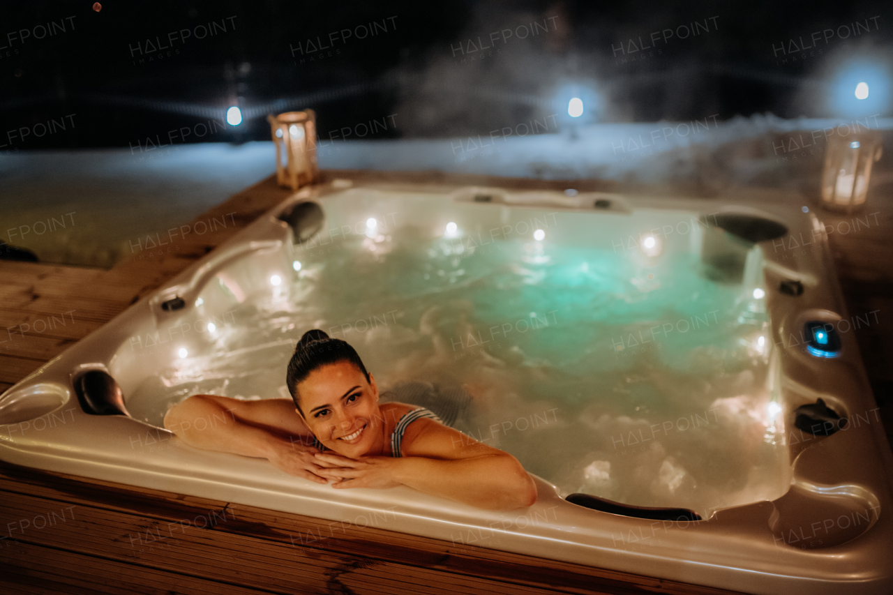 Young woman enjoying outdoor bathtub in her terrace during a cold winter evening.