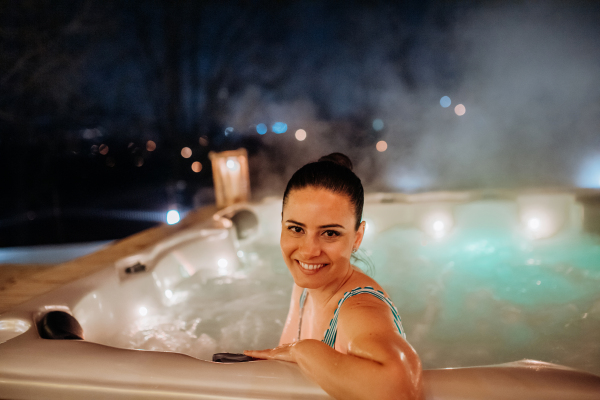 Young woman enjoying outdoor bathtub in her terrace during a cold winter evening.