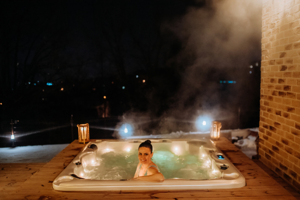 Young woman enjoying outdoor bathtub in her terrace during a cold winter evening.