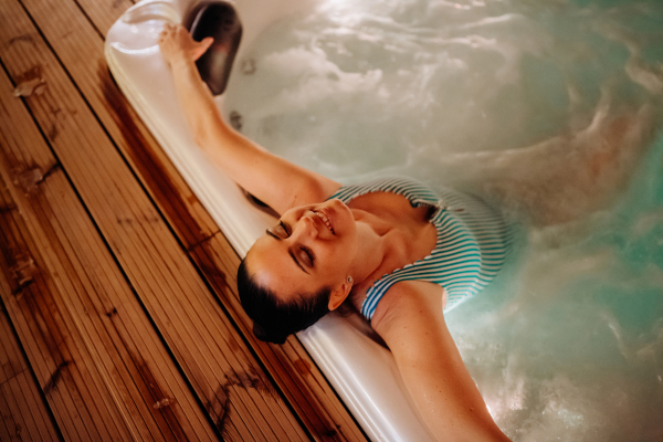 Young woman enjoying outdoor bathtub in her terrace during a cold winter evening.