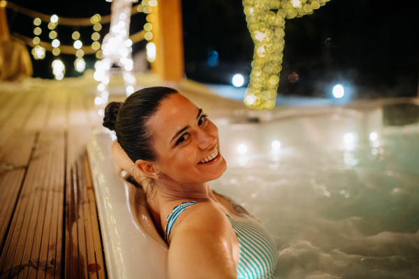 Young woman enjoying outdoor bathtub in her terrace during a cold winter evening.