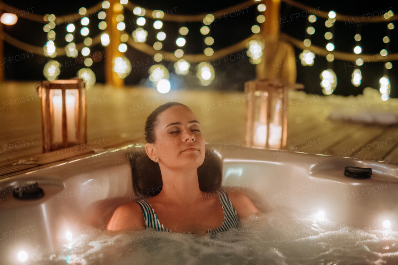 Young woman enjoying outdoor bathtub in her terrace during a cold winter evening.