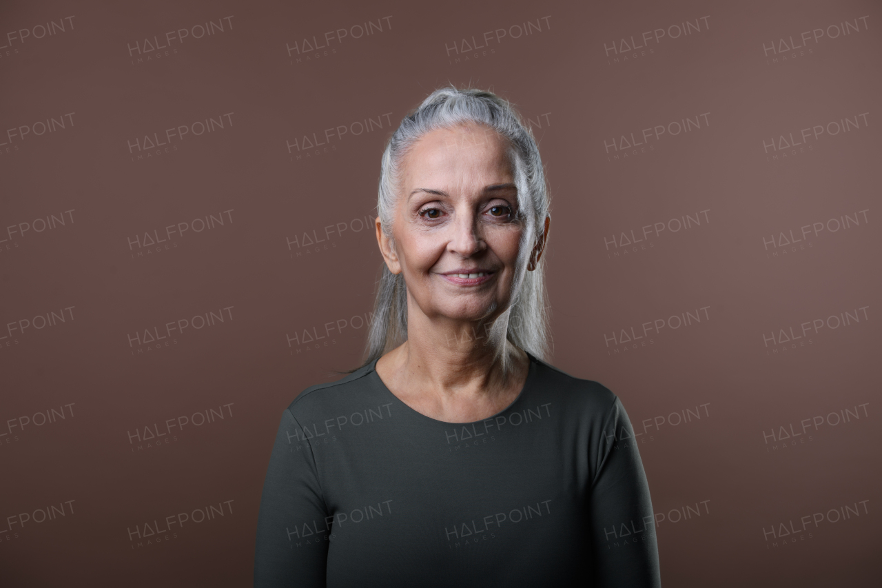 Studio portrait of beautiful senior woman with long gray hair in ponytail. Isolated on a brown pink background. Copy space.