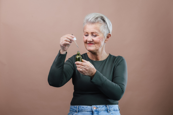 Portrait of smiling senior woman holding skincare serum drops in bottle.Concept of beauty and skincare.