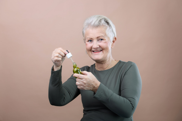 Portrait of smiling senior woman holding skincare serum drops in bottle.Concept of beauty and skincare.