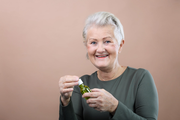 Portrait of smiling senior woman holding skincare serum drops in bottle.Concept of beauty and skincare.