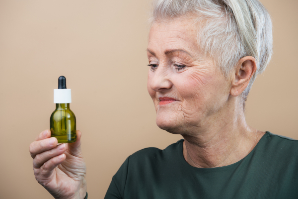 Portrait of smiling senior woman holding skincare serum drops in bottle.Concept of beauty and skincare.