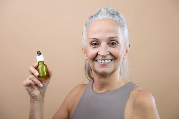 Portrait of smiling senior woman holding skincare serum drops in bottle.Concept of beauty and skincare.