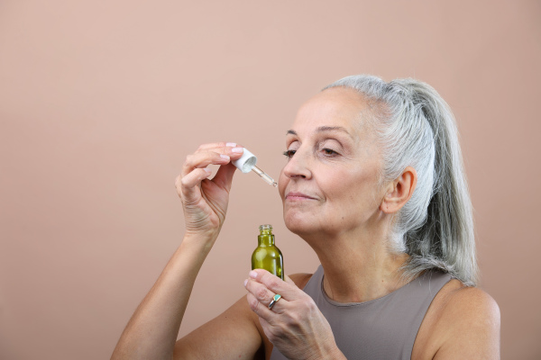 Portrait of smiling senior woman holding skincare serum drops in bottle.Concept of beauty and skincare.