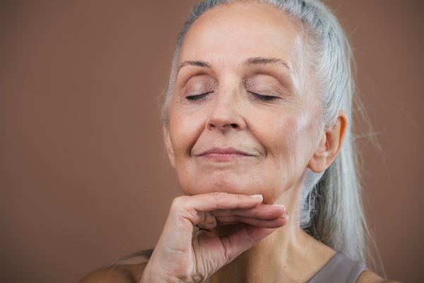 Studio portrait of beautiful senior woman with long gray hair, closed eyes. Isolated on a brown pink background. Copy space.